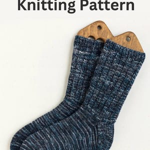 May include: A pair of adult socks, knitted with blue, white, and grey speckled yarn. The socks are displayed on wooden sock forms. The text "Adult Socks Knitting Pattern" is at the top.