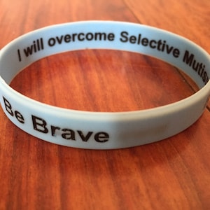 May include: A light blue silicone bracelet with the text "I will overcome Selective Mutism. Be Brave" printed in black.