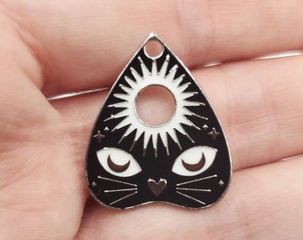 May include: Black and white charm shaped like a witch's board or planchette with a cat face and a sun in the centre.