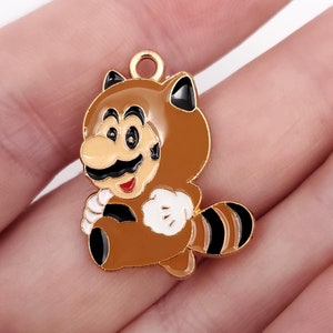 May include: Gold-tone metal charm featuring a cartoon character wearing a brown raccoon costume. The character has a black mustache and a red mouth. The charm has a loop at the top for attaching to a necklace or bracelet.