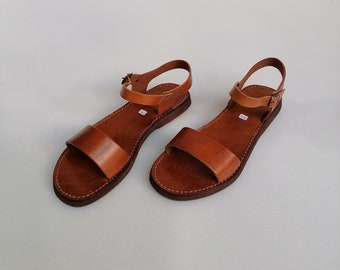 May include: A pair of brown leather sandals with ankle straps and buckles. The sandals have a simple design and are perfect for summer.