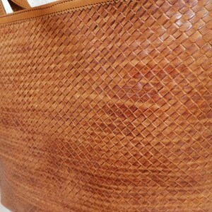 Op de afbeelding: Een bruine leren tote bag met een geweven patroon. De tas heeft een bovenste handvat en twee schouderbanden.