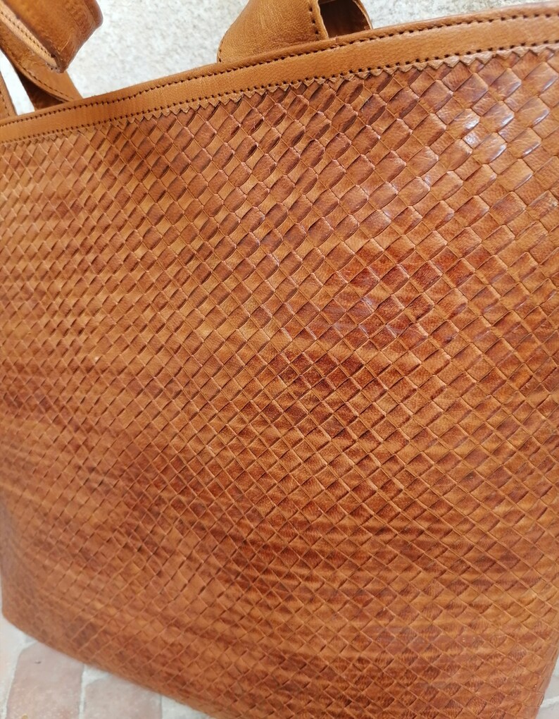 Op de afbeelding: Een bruine leren tote bag met een geweven patroon. De tas heeft een bovenste handvat en twee schouderbanden.