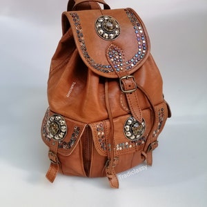 Può includere: Uno zaino in pelle marrone con borchie metalliche decorative e una grande fibbia in metallo. Lo zaino ha due tasche anteriori e una chiusura con coulisse.