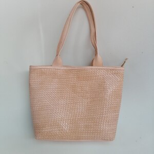 Op de afbeelding: Een lichtbeige geweven tote bag met twee handvatten.