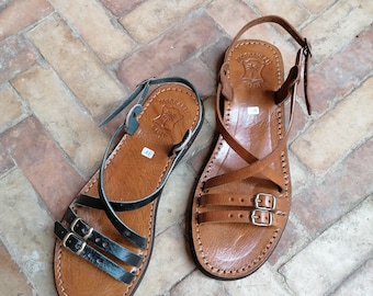 May include: A pair of brown leather sandals with black straps and double buckles. The sandals have a  "Marrakech" brand label on the straps.
