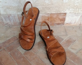 May include: A pair of brown leather sandals with multiple straps. The sandals have a buckle closure and a comfortable, flat sole.