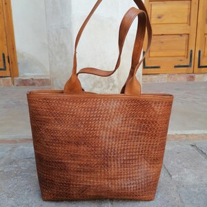 Op de afbeelding: Een bruine leren tote bag met een geweven patroon. De tas heeft twee hengsels en een ritssluiting.