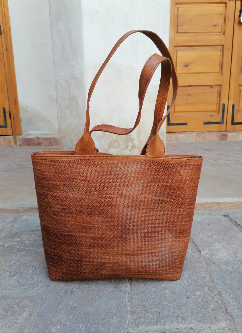 Op de afbeelding: Een bruine leren tote bag met een geweven patroon. De tas heeft twee hengsels en een ritssluiting.