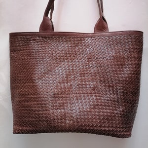 Op de afbeelding: Een bruine leren tote bag met een geweven patroon. De tas heeft twee bovenste handvatten.