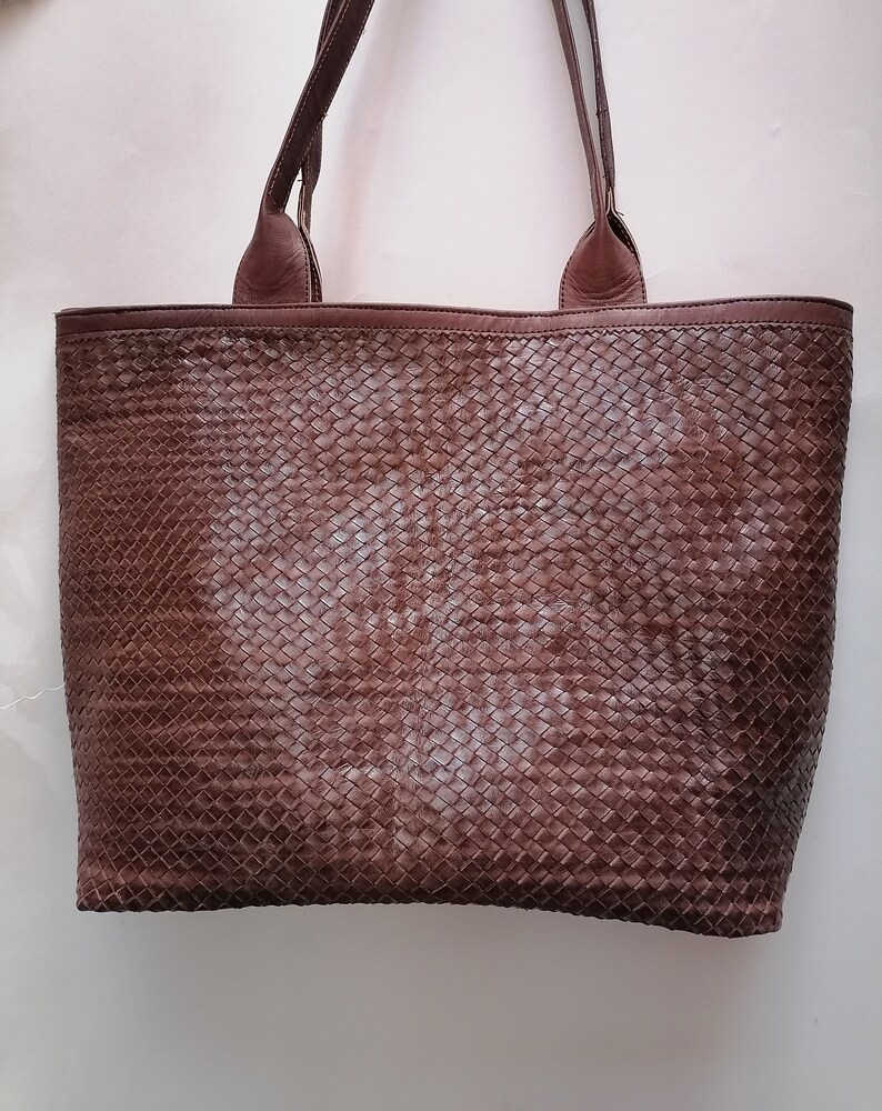 Op de afbeelding: Een bruine leren tote bag met een geweven patroon. De tas heeft twee bovenste handvatten.
