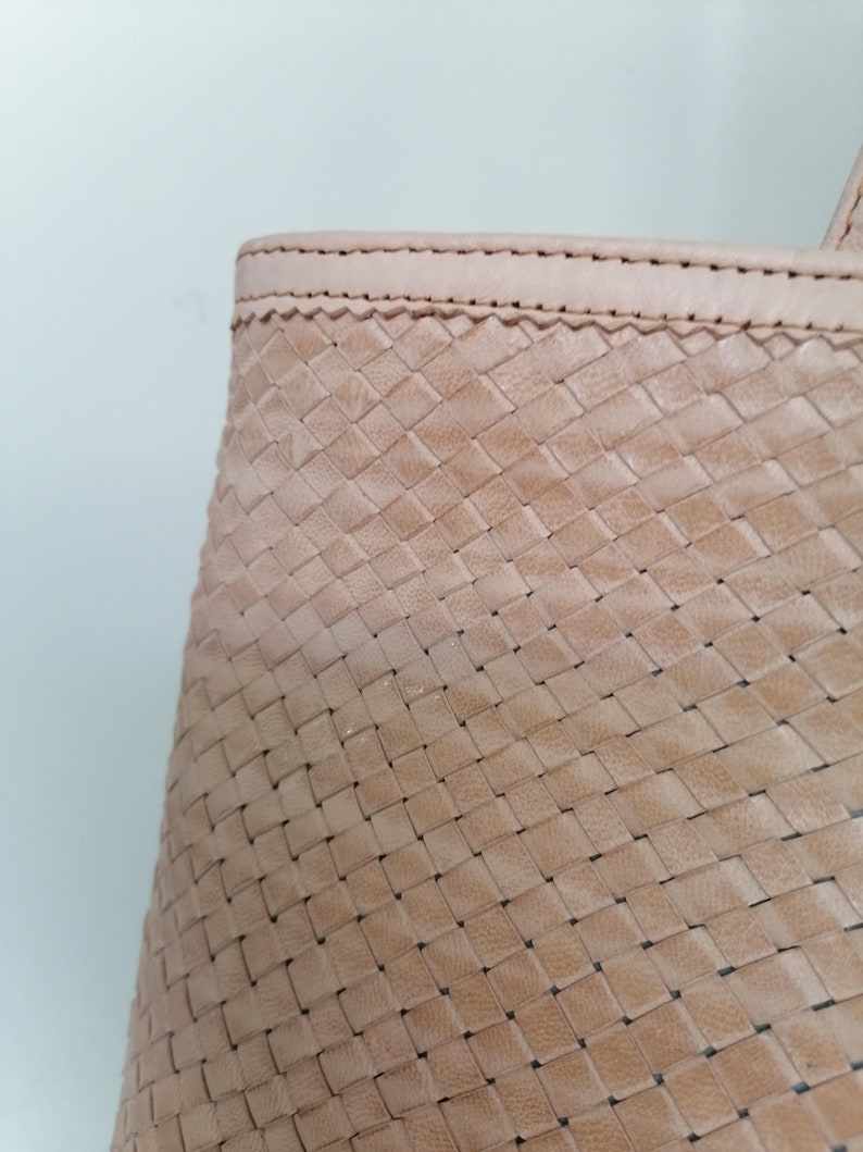 Op de afbeelding: Close-up van een lichtbruine geweven leren tote bag. De tas heeft een gestikte naad rond de bovenrand.