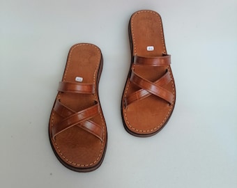 May include: A pair of brown leather sandals with criss-cross straps. The sandals have a simple design and are made of high-quality leather.