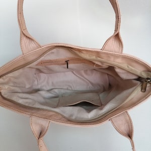 Op de afbeelding: Een lichtroze leren tote bag met twee bovenste handvatten. De tas is open en de binnenkant is gevoerd met een lichtbeige stof. Er zit een klein ritsvakje aan de binnenkant van de tas.