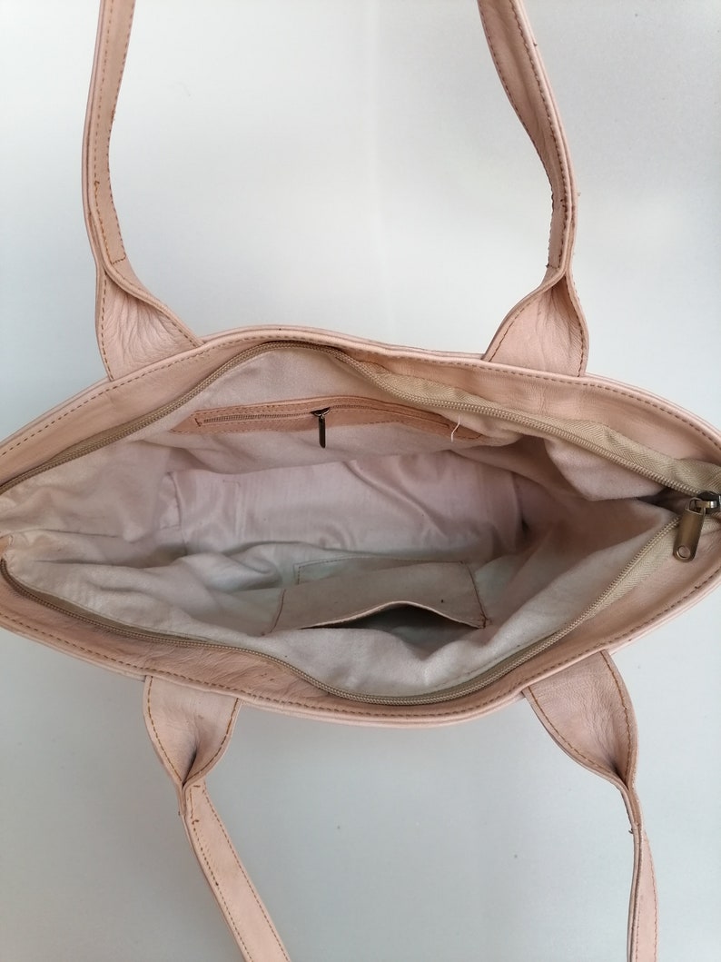 Op de afbeelding: Een lichtroze leren tote bag met twee bovenste handvatten. De tas is open en de binnenkant is gevoerd met een lichtbeige stof. Er zit een klein ritsvakje aan de binnenkant van de tas.