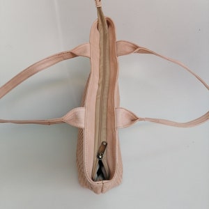 Op de afbeelding: Een lichtroze leren tote bag met een ritssluiting. De tas heeft twee hengsels en is open om het interieur te laten zien.