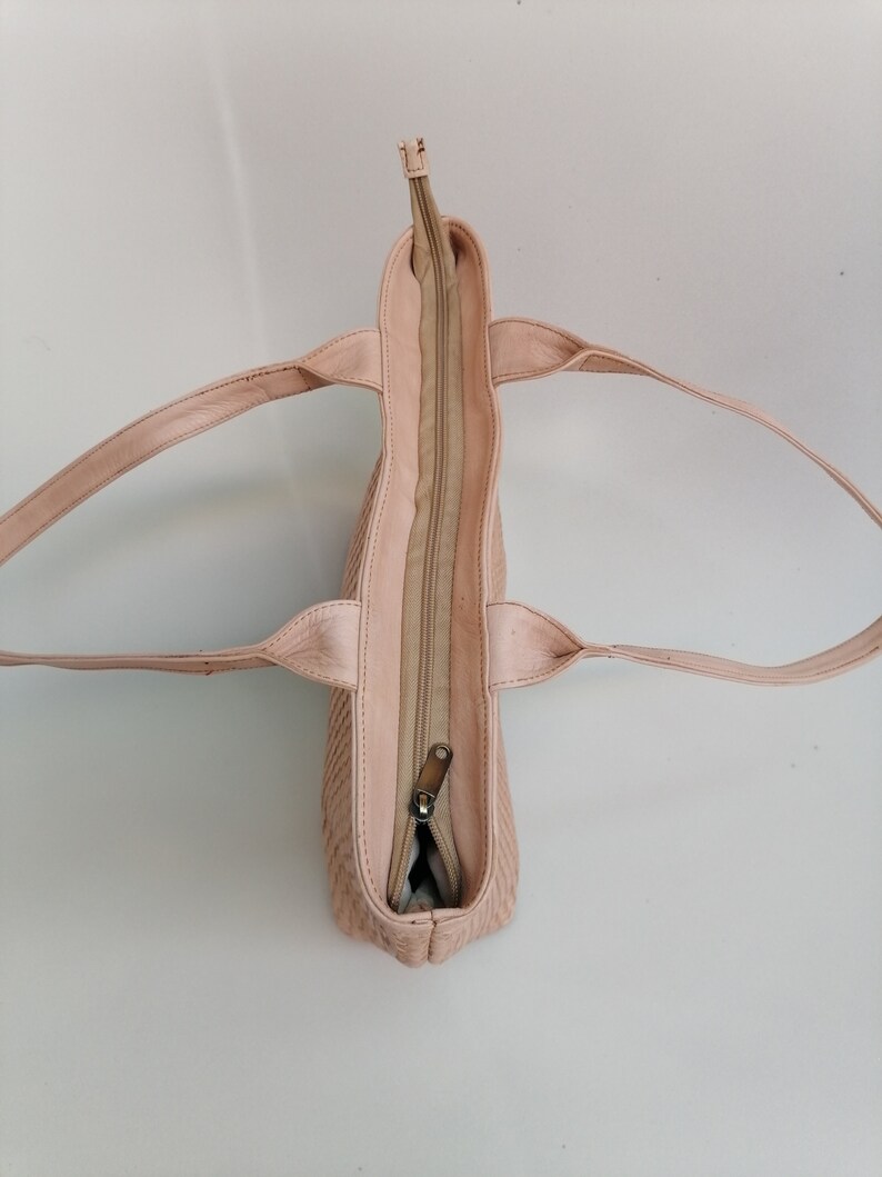 Op de afbeelding: Een lichtroze leren tote bag met een ritssluiting. De tas heeft twee hengsels en is open om het interieur te laten zien.