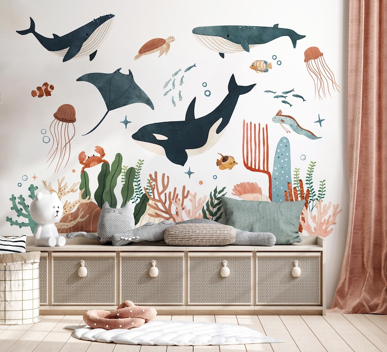 May include: A whimsical wall mural featuring watercolor illustrations of marine life, including whales, a manta ray, and jellyfish. The design incorporates coral, seaweed, and other underwater elements, creating a vibrant and playful ocean theme. A storage bench with decorative pillows and a rug is in the foreground.
