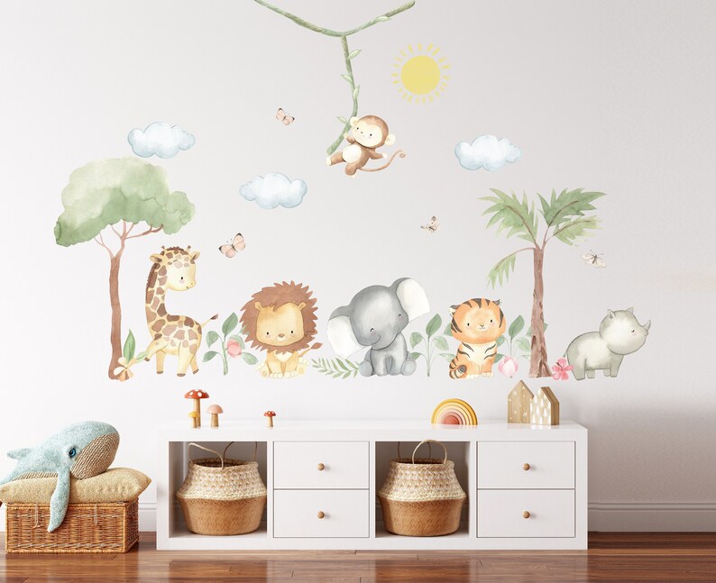 Puede incluir: Un conjunto de calcoman&iacute;as de animales de acuarela para pared que incluyen una jirafa, un le&oacute;n, un elefante, un tigre y un rinoceronte. Las calcoman&iacute;as est&aacute;n dispuestas en una l&iacute;nea en una pared blanca, con una palmera y un mono colgado de una enredadera encima. Las calcoman&iacute;as son perfectas para una guarder&iacute;a o una habitaci&oacute;n infantil.