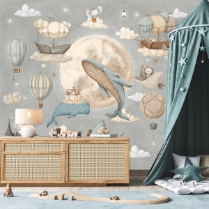 Puede incluir: Una escena de guarder&iacute;a caprichosa con un mural gris que representa una luna, ballenas, globos aerost&aacute;ticos y nubes. Debajo, un aparador de madera con una l&aacute;mpara y juguetes. Un dosel turquesa con detalles de estrellas a&ntilde;ade un toque de ensue&ntilde;o.