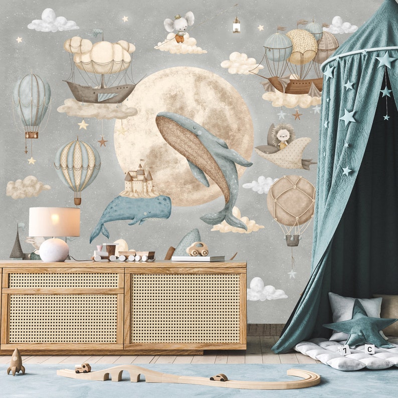 Puede incluir: Una escena de guarder&iacute;a caprichosa con un mural gris que representa una luna, ballenas, globos aerost&aacute;ticos y nubes. Debajo, un aparador de madera con una l&aacute;mpara y juguetes. Un dosel turquesa con detalles de estrellas a&ntilde;ade un toque de ensue&ntilde;o.