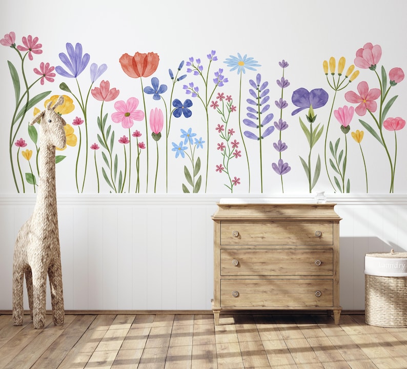 May include: A wall decal featuring a vibrant watercolour floral design with various colourful flowers, including red poppies, pink, purple, and blue blooms. A woven giraffe and a wooden dresser are in the foreground.