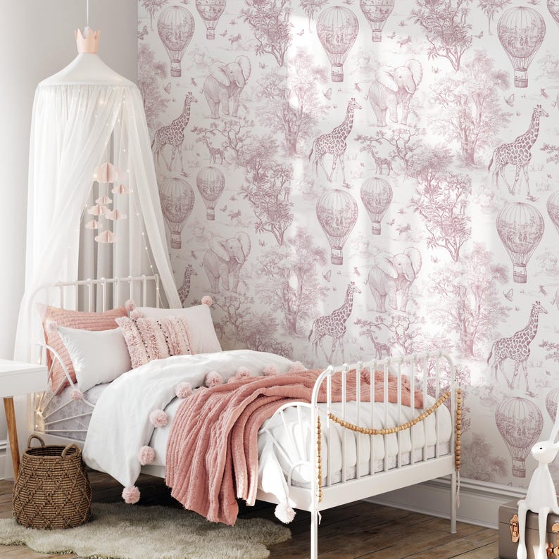 May include: A child's bedroom with a white metal bed, canopy, and a pink and white color scheme. The bed is adorned with pillows, a white duvet, and a pink throw blanket. The wallpaper features a safari theme with giraffes, elephants, and hot air balloons.