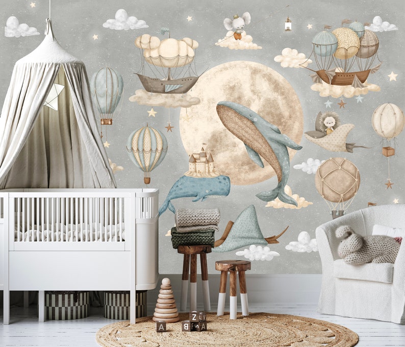 Puede incluir: Una escena de guarder&iacute;a caprichosa con un mural que representa una luna, globos aerost&aacute;ticos y ballenas en tonos pastel. Una cuna blanca, un dosel, un taburete de madera y mantas completan la escena. El ambiente es on&iacute;rico.
