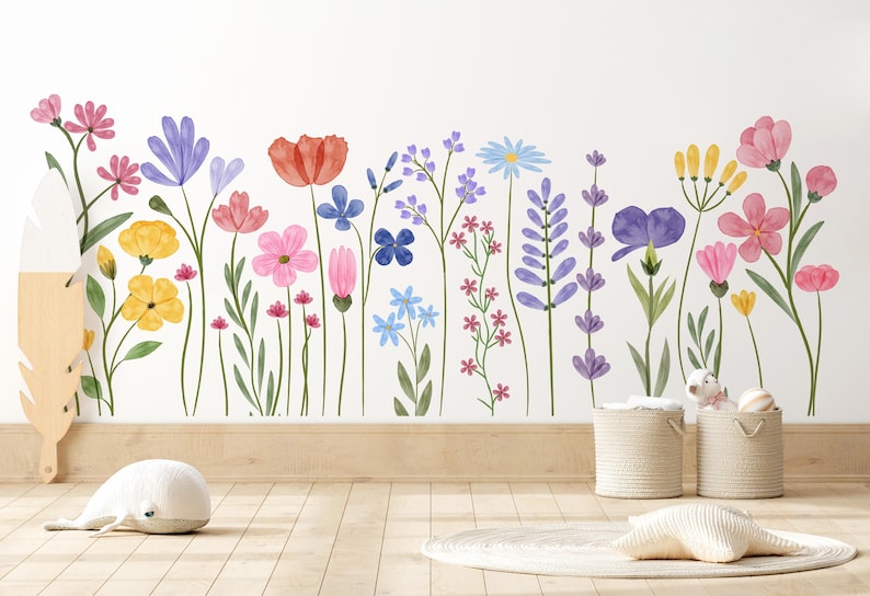 May include: A vibrant floral wall sticker showcasing watercolour flowers in pink, purple, yellow, and blue. The sticker is on a white wall, with a wooden floor and decorative items in the foreground. The flowers are in full bloom.