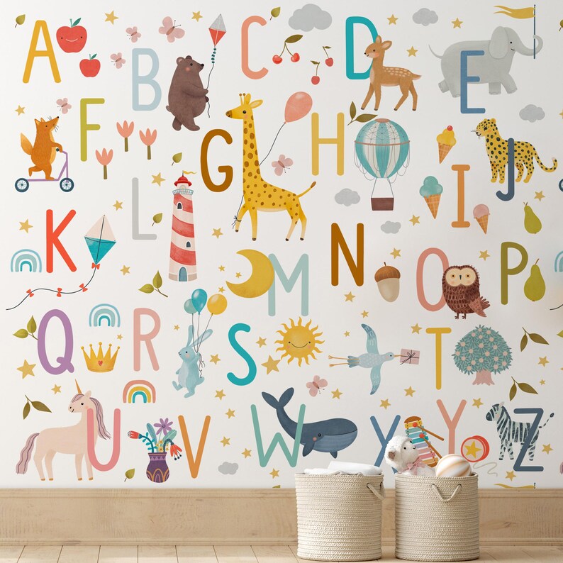 May include: A whimsical wall mural featuring the alphabet with colorful illustrations of animals and objects. The design includes a giraffe, bear, deer, and a unicorn, along with a hot air balloon, kite, and ice cream cones. The letters are in various colors against a white background.
