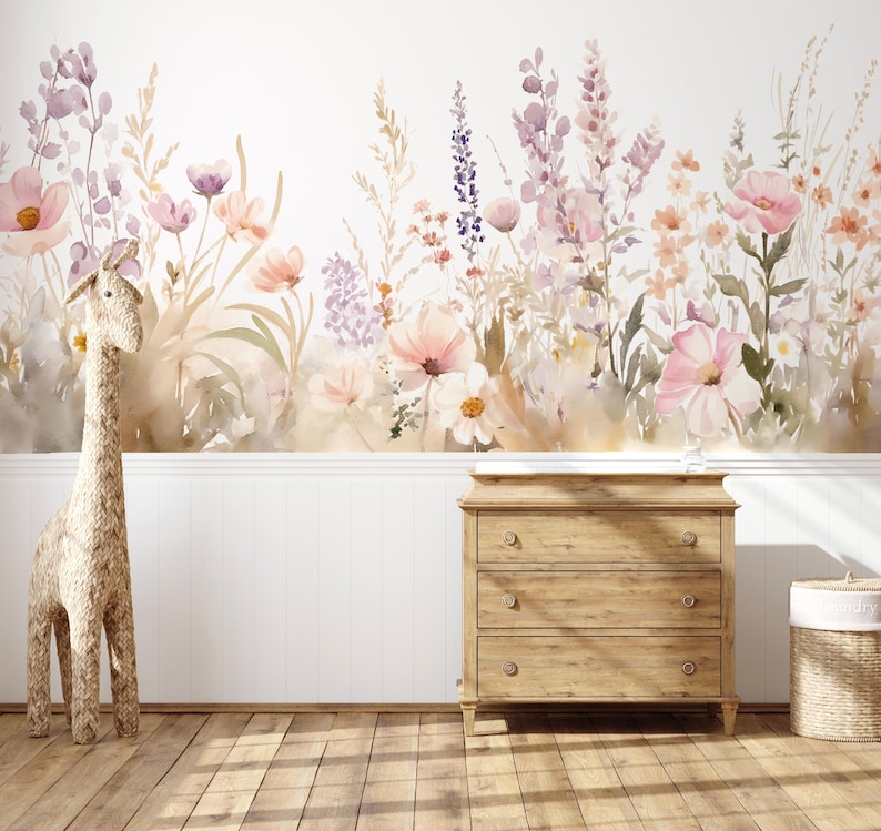 以下が含まれることがあります： パステルカラーの花柄壁画のある子供部屋のシーン。編み込みのキリンが木製のドレッサーの近くに立っています。ふた付きの編み込みバスケットが右側にあります。部屋には木の床と白い腰壁があります。