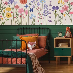 May include: A bedroom with a black metal bed, rust-coloured bedding, orange and green cushions, and a green blanket. A fox toy sits on the bed. The wall features a floral mural with watercolour flowers. A wooden bedside table with a green drawer and a clock is visible.