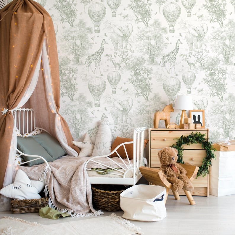 Puede incluir: Un dormitorio infantil con una cama de metal blanco, un dosel marr&oacute;n con luces de hadas y una c&oacute;moda. El papel pintado presenta una escena de safari con elefantes, jirafas y globos aerost&aacute;ticos. Accesorios como un oso de peluche y cojines.
