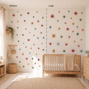 Puede incluir: Un conjunto de pegatinas de pared con formas de estrellas multicolores en rojo, verde, azul y dorado sobre una pared blanca. La muestra est&aacute; dividida en dos secciones etiquetadas como Medium y Large, con una cuna de madera frente a la pared.