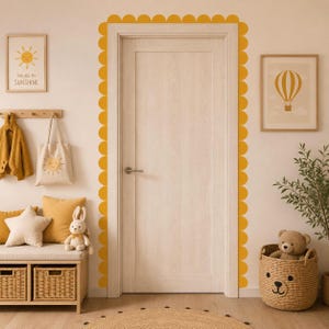 May include: A bright, inviting interior scene with a wooden door framed by yellow scalloped trim. The room features a bench with pillows and a stuffed bunny, a tote bag with a sun graphic, and framed artwork. The text on the artwork says "YOU ARE MY SUNSHINE".