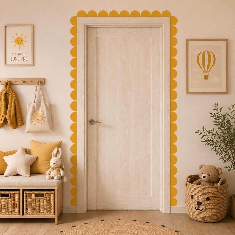 May include: A bright, inviting interior scene with a wooden door framed by yellow scalloped trim. The room features a bench with pillows and a stuffed bunny, a tote bag with a sun graphic, and framed artwork. The text on the artwork says "YOU ARE MY SUNSHINE".
