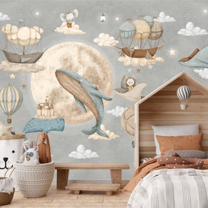 Puede incluir: Un mural caprichoso para la habitaci&oacute;n infantil con una ballena, globos aerost&aacute;ticos y dirigibles flotando en un cielo estrellado. El dise&ntilde;o incluye una gran luna, nubes y un marco de cama de madera con forma de casa. Tambi&eacute;n se ven cestas decorativas y animales de peluche.