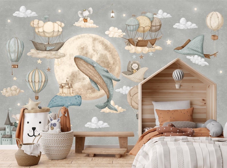 Puede incluir: Un mural caprichoso para la habitaci&oacute;n infantil con una ballena, globos aerost&aacute;ticos y dirigibles flotando en un cielo estrellado. El dise&ntilde;o incluye una gran luna, nubes y un marco de cama de madera con forma de casa. Tambi&eacute;n se ven cestas decorativas y animales de peluche.