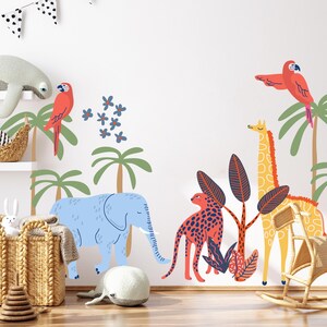 Op de afbeelding: Een muursticker set met een lichtblauwe olifant, een gele giraf, een rode luipaard en twee rode papegaaien. Het ontwerp bevat groene palmbomen en blauwe bloemen, wat een kleurrijke jungle-sc&egrave;ne cre&euml;ert voor op de muur.