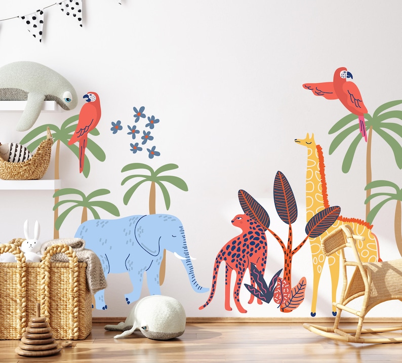 Op de afbeelding: Een muursticker set met een lichtblauwe olifant, een gele giraf, een rode luipaard en twee rode papegaaien. Het ontwerp bevat groene palmbomen en blauwe bloemen, wat een kleurrijke jungle-sc&egrave;ne cre&euml;ert voor op de muur.