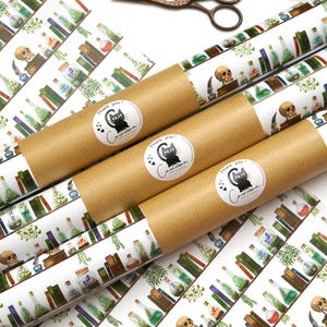 Könnte beinhalten: Dekorative Geschenkpapierrollen mit einem sich wiederholenden Muster aus Zaubertränken, Büchern und Totenköpfen. Die Rollen sind mit einem Aufkleber mit einer schwarzen Katze und dem Text "Thank you!" versehen. Eine bronzefarbene Schere liegt in der Nähe.