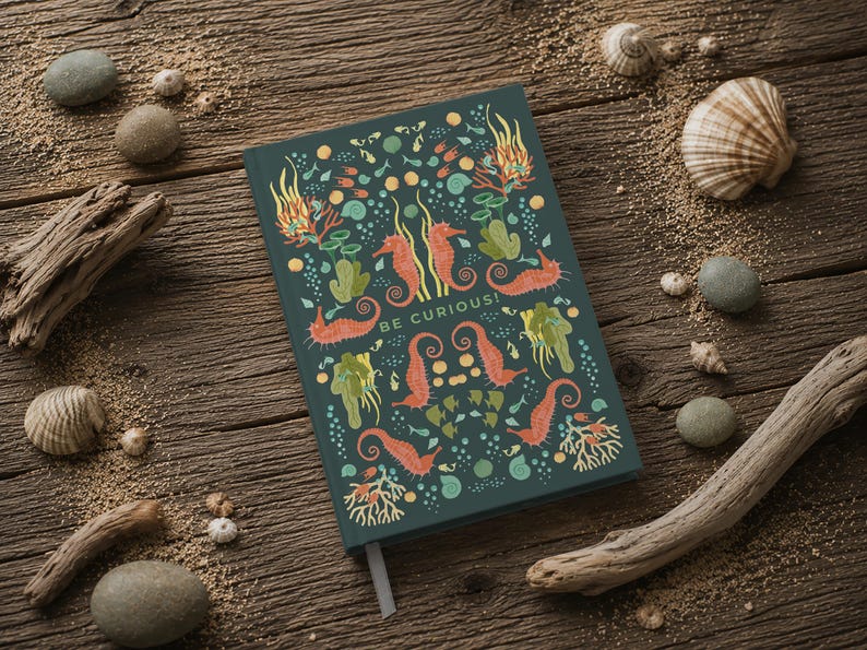 May include: A teal notebook with a seahorse and sea life design. The cover features orange seahorses, green seaweed, and the words "BE CURIOUS!". The notebook is on a wooden surface with seashells and driftwood.