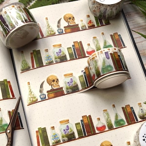 Könnte beinhalten: Dekoratives Washi-Tape mit einem sich wiederholenden Muster von Regalen mit Büchern, Zaubertränken, Totenköpfen und Gläsern mit Pflanzen. Das Tape ist gerollt und teilweise abgerollt. Der Hintergrund ist ein weißer, gepunkteter Untergrund.