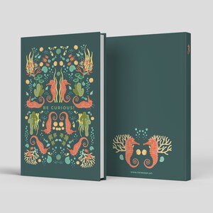 May include: A teal notebook with a colorful seahorse and coral design. The cover features the words "BE CURIOUS!" and the back has a matching seahorse and coral design. The notebook is a hardcover style.