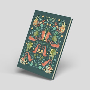 May include: A teal journal with a colorful sea-themed design. The cover features orange seahorses, coral, and seaweed illustrations, with the words "BE CURIOUS!" in white. The journal has a cream-colored spine and a hard cover.