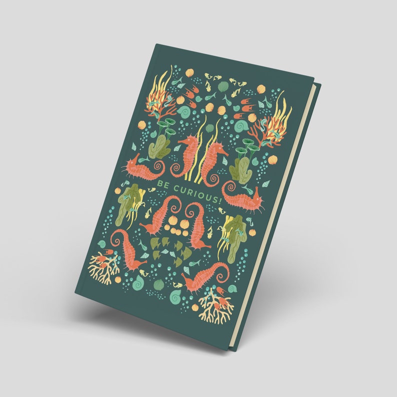 May include: A teal journal with a colorful sea-themed design. The cover features orange seahorses, coral, and seaweed illustrations, with the words "BE CURIOUS!" in white. The journal has a cream-colored spine and a hard cover.