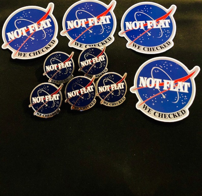 May include: A set of eight stickers and pins featuring a blue and red graphic of a rocket ship with the text "NOT FLAT WE CHECKED".