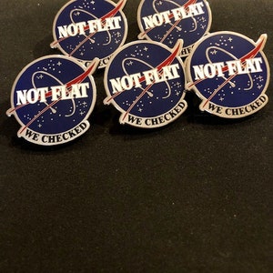 May include: Five silver pins with a blue and white NASA-style logo. The logo says "NOT FLAT WE CHECKED" in white text.