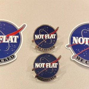 May include: Three blue and white stickers with the text "NOT FLAT WE CHECKED" and a red and white rocket design. Two smaller blue and white pins with the same text and design.