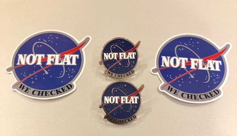 May include: Three blue and white stickers with the text "NOT FLAT WE CHECKED" and a red and white rocket design. Two smaller blue and white pins with the same text and design.